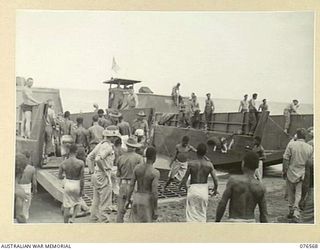 HOSKINS, NEW BRITAIN. 1944-10-09. NATIVES ASSISTING PERSONNEL OF THE 36TH INFANTRY BATTALION TO UNLOAD STORES AND EQUIPMENT FROM LANDING BARGES DRAWN UP ON THE BEACH