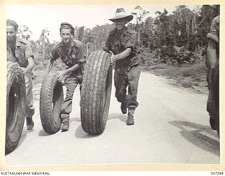 WEWAK AREA, NEW GUINEA. 1945-10-13. MEMBERS OF 3 MOBILE TYRE WORKSHOP SECTION WHEELING SALVAGED JAPANESE TYRES UP THE ROAD TO LOAD THEM ONTO TRUCKS