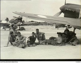 KIRIWINA, TROBRIAND ISLANDS, PAPUA. 1943-11-12. FITTERS, ARMOURERS AND RIGGERS OF NO. 76 SQUADRON RAAF RESTING UNDER THE WING OF A KITTYHAWK FIGHTER AIRCRAFT