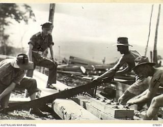 JACQUINOT BAY, NEW BRITAIN. 1945-01-24. TROOPS OF THE 17TH FIELD COMPANY, SAWING AND BOLTING TOGETHER TIMBER TO FORM THE HEADSTOCK FOR THE STRINGERS OF THE NEW 300 FOOT WHARF WHICH THEY ARE ..