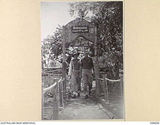 MALAGUNA, NEW BRITAIN. 1945-11-06. CORPORAL G. BROWN (1), AND CORPORAL H. GRILLS (2), MEMBERS OF 11 DIVISION PROVOST DETACHMENT PASSING THROUGH THE ENTRANCE ARCHWAY TO THE PROVOST CORPS QUARTERS AT ..