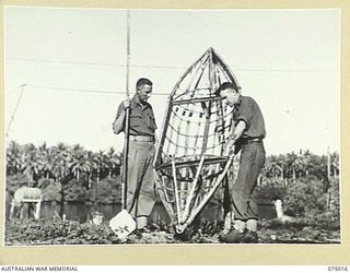 MILILAT, NEW GUINEA. 1944-08-01. TWO NON COMMISSIONED OFFICERS OF HEADQUARTERS, 5TH DIVISION, FIELD CASH OFFICE PROUDLY DISPLAY THE BAMBOO FRAMEWORK OF A CANOE WHICH THEY ARE BUILDING IN THEIR ..