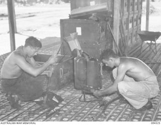 TOROKINA, BOUGAINVILLE. 1945-07-25. CORPORAL A. FLYNN (1) AND SERGEANT R.B. DUNKLEY (2), MEMBERS OF 16 ADVANCED ORDNANCE DEPOT CHECKING A FLAME-THROWER PRIOR TO ISSUE