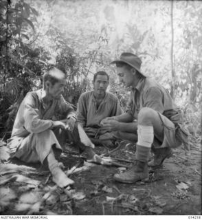 SANANANDA, PAPUA. 1943. AN AUSTRALIAN, PROBABLY FROM 2/7TH CAVALRY REGIMENT, WOUNDED ON THE LEG, ROLLS A CIGARETTE FOR A JAPANESE PRISONER CAPTURED AT SANANANDA