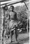 Boy by house frame, holding taro plant