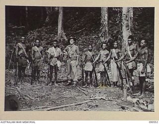 WONGINARA MISSION, NEW GUINEA. 1945-04-06. WARRANT OFFICER 2 JOHN BORRIT GODWIN, AUSTRALIAN NEW GUINEA ADMINISTRATIVE UNIT PATROL OFFICER (FOURTH FROM LEFT), WITH SOME OF HIS GUERILLAS. HIS SELF ..