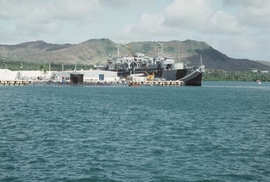 The submarine tender USS PROTEUS (AS-19) and an unidentified submarine stand moored to the pier at the naval station. The PROTEUS' World War II camouflage pattern was added for the ship's visit to Australia for the ceremonies commemorating the 50th anniversary of the Battle of the CORAL SEA