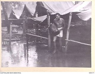 BOUGAINVILLE. 1945-07-19. SERGEANT K.J. MCHARRIE WADING THROUGH THE STORE AS MEMBERS OF Q STAFF, 29 INFANTRY BRIGADE, SALVAGE EQUIPMENT AFTER FLOODING. DURING THE LAST FIVE DAYS, SEVEN INCHES OF ..