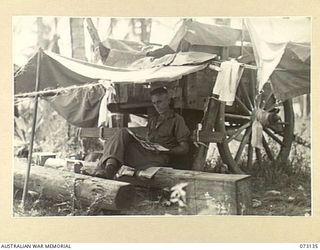 ALEXISHAFEN, NEW GUINEA. 1944-05-11. NX131591 PRIVATE N. KELLY, 35TH INFANTRY BATTALION, RELAXES UNDER A SHELTER RIGGED TO AN ABANDONED JAPANESE CART