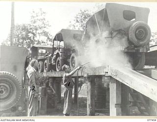 LAE BASE AREA, NEW GUINEA. 1944-12-04. CRAFTSMAN J.I.M. SIM OF THE 2/77TH LIGHT AID DETACHMENT SPRAYING A JEEP WITH RUST INHIBITOR WATCHED BY DRIVER A. LUDKIN