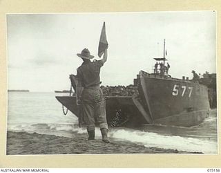 TSIMBA AREA, BOUGAINVILLE ISLAND. 1945-02-21. NX1400 CAPTAIN C.T. COLQUHOUN, OFFICER- IN- CHARGE, PUTO BEACH, GUIDING LANDING CRAFT ASHORE. THESE CRAFT ARE BRINGING TROOPS OF THE 26TH INFANTRY ..