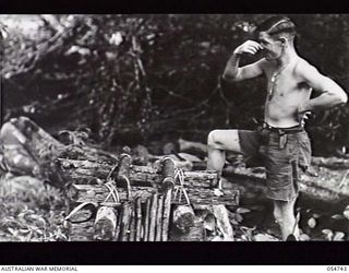 BULLDOG ROAD, NEW GUINEA. 1943-07-10. SX2663 SERGEANT E. E. SMITH ELOQUENTLY SHOWS HIS DISAPPROVAL OF AN IMPROVISED TOILET AT THE 7 MILE POST