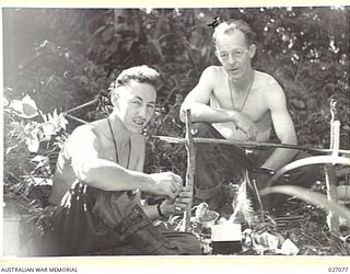 PAPUA, NEW GUINEA. 1942-10. TWO OF THE 25TH AUSTRALIAN INFANTRY BRIGADE SIGNALLERS, SIGNALLER G.W. HAY, (LEFT) AND SIGNALLER G.B. DEAN, MAKE THEIR MEAL OVER A SMALL FIRE IN THE JUNGLE NEAR MENARI