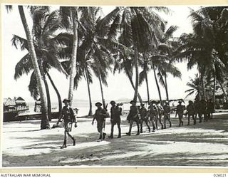 PAPUA, NEW GUINEA. 1942-07. AN AUSTRALIAN INFANTRY PATROL PASSING BY A PAPUAN COASTAL VILLAGE AND THROUGH A COCONUT GROVE