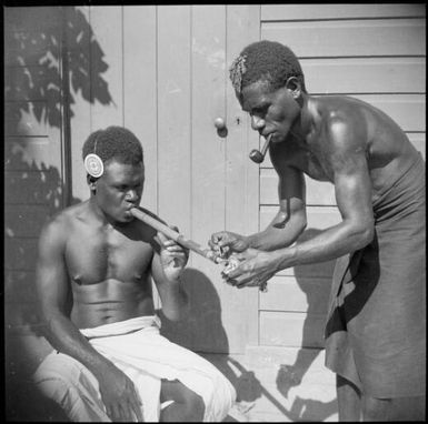 Aiau, the Chinnery's garden boy, lighting a bamboo pipe for Asavia, Malaguna Road, Rabaul, New Guinea, ca. 1936, 2 / Sarah Chinnery