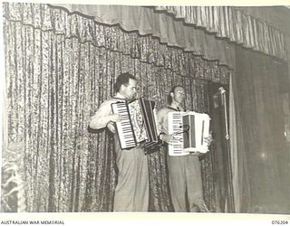 LAE, NEW GUINEA. 1944-09-26. SERGEANT GOLDSMITH (1), AND CORPORAL R. RUDLEIGH (2), PLAYING AN ACCORDION DUET DURING A CONCERT STAGED BY THE "TANKS A MILLION CONCERT PARTY" AT THE OFFICIAL OPENING ..