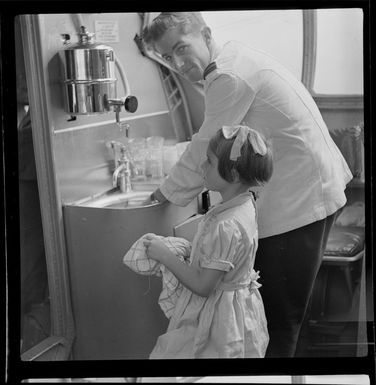 Young child Jennifer Gray, a passenger on Qantas Catalina flying boat service from Suva, Fiji, to Sydney, Australia, helping steward R White with the dishes