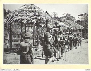 PAPUA, NEW GUINEA. 1942-10. MEN OF THE 2/33RD AUSTRALIAN INFANTRY BATTALION MARCHING THROUGH THE SMALL NATIVE VILLAGE OF NAURO ON THEIR WAY THROUGH THE OWEN STANLEY RANGES TO KOKODA