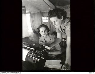 Port Moresby, New Guinea. 1944-05-29. Sergeant E. M. Hawkes, sitting behind a typewriter, and Lance Corporal K. Wells, members of Australian Army Medical Womens Service (AAMWS) working in the ..