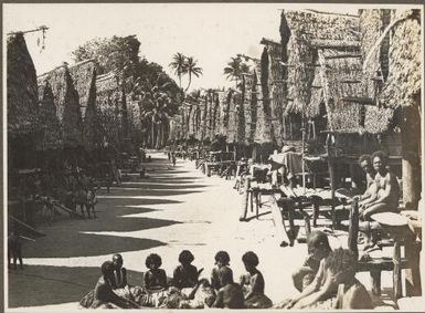 Scene in  Mailu Village, [women sitting in a circle on the path between the rows of huts, Papua New Guinea]