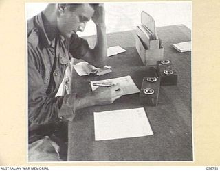 KARAWOP, NEW GUINEA, 1945-09-18. TPR W.G. POLLARD, 2/6 CAVALRY COMMANDO REGIMENT, TRYING TO CONCENTRATE ON LETTER WRITING