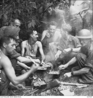 PAPUA, NEW GUINEA. 1942-10. SOLDIERS OF THE 2/31ST AUSTRALIAN INFANTRY BATTALION HEAT UP THEIR FRUGAL MEAL OF BULLY BEEF AND BISCUITS ALONG THE TRACK OVER THE OWEN STANLEY RANGES NEAR MENARI