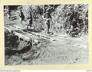 BOUGAINVILLE ISLAND. 1945-02-13. VX37706 WARRANT OFFICER II, H. ROBERTS, NEW GUINEA ADMINISTRATION UNIT, CROSSING A SMALL FOOTBRIDGE AS HE RETURNS TO CAMP WITH HIS NATIVE CARRIERS AND MEMBERS OF ..