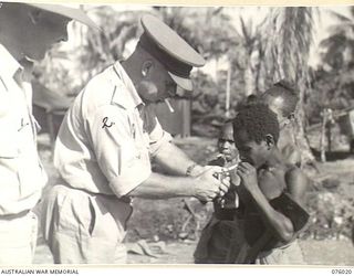 LAE, NEW GUINEA. 1944-09-18. TX2002 BRIGADIER J. FIELD, DSO, ED, COMMANDING, 7TH INFANTRY BRIGADE (2) LIGHTS A CIGARETTE FOR ONE OF THE NATIVE BOYS WHO ESCORTED HIMSELF AND HIS PARTY BACK TO TSILI ..