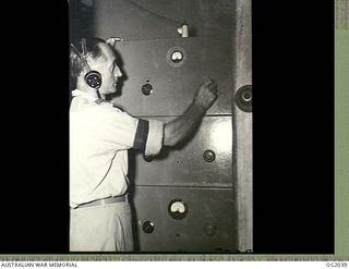 MADANG, NEW GUINEA. C. 1944. FLIGHT LIEUTENANT J. E. PARRIS, SIGNALS AND RADAR OFFICER, THE CHIEF ENGINEER AT RAAF RADIO MADANG, IS CHECKING THE TUNING OF THE STATION'S MODERN 250 WATT TRANSMITTER