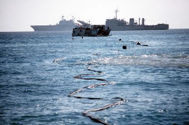 A utility landing craft (LCU-1664) approaches the tank landing ship USS BARNSTABLE COUNTY (LST-1197) for the attachment of a ship-to-shore fuel line during Exercise Crisex '81. The amphibious assault ship USS SAIPAN (LHA-2) is also visible in the background