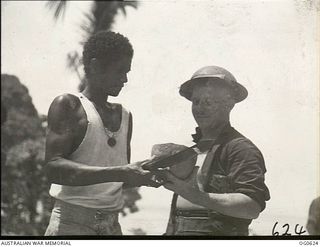 KIRIWINA, TROBRIAND ISLANDS, PAPUA. 1944-01-31. AIRCRAFTMAN 1 A. R. HILL OF MONTO, QLD (RIGHT), HAS BEEN ADOPTED AS FRIEND BY LOCAL NATIVE KATULOKA, WHO IS SHOWN CARVING UP A COCONUT FOR HIS RAAF ..