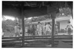 Group carrying feast items, including trussed pig