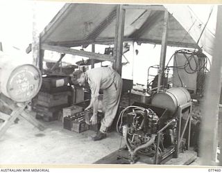 LAE BASE AREA, NEW GUINEA. 1944-12-04. NX20506 CORPORAL M. CHISHOLM, ELECTRICIAN, 2/77TH LIGHT AID DETACHMENT, CHECKING BATTERIES BEING CHARGED ON A HOWARD 5KVA GENERATING SET IN THE UNIT ..