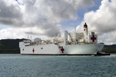 The US Navy Military Sealift Command (MSC) Mercy Class Hospital Ship (AH) USNS MERCY is guided by a tugboat (right) as it enters Apra Harbor, Guam, during its five-month deployment in the Pacific Region. The ship will participate in humanitarian assistance and civic action programs with civilian organizations at several Western Pacific islands. The MERCY is capable of supporting medical and humanitarian assistance needs. It is configured with special medical equipment and the ship has multi-specialized medical teams that can provide a range of services ashore as well as aboard the vessel