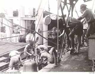 MANUS HARBOUR, ADMIRALTY ISLANDS. 1945-07-05. LIEUTENANT CARTWRIGHT, FIRST OFFICER OF HMAS NEPAL, WATCHES WHILE CREW MEMBERS UNLOAD AMMUNITION FROM A SUPPLY VESSEL. THE AUSTRALIAN DESTROYER WAS ..