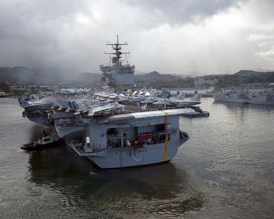 A stern view of the nuclear-powered aircraft carrier USS ENTERPRISE (CVN 65) as a harbor tug assists it into its berth at Pearl Harbor