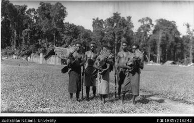 Five men, two with rifles and the other three with large birds, probably Victoria Crowned Pigeons