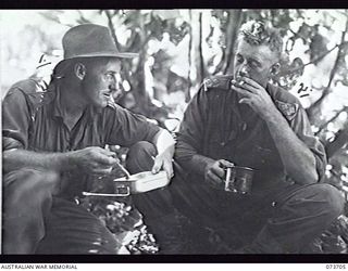 BUNABUN, NEW GUINEA. 1944-05-28. NX157290 WARRANT OFFICER 2 L. G. HAGEN (LEFT) AND NX156376 LIEUTENANT E. THEW, MEMBERS OF 35TH INFANTRY BATTALION, RESTING AND ENJOYING A MEAL DURING A PAUSE IN THE ..