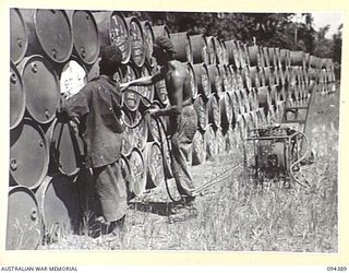 LAE AREA, NEW GUINEA. 1945-07-12. CORPORAL H.C. MARSHALL, 2 BULK PETROLEUM STORAGE COMPANY, OPERATING THE STENCILLING PLANT TO MARK DRUMS. THREE THOUSAND 44-GALLON DRUMS ARE TURNED OUT DAILY BY THE ..