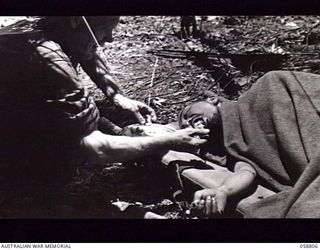 DUMPU, NEW GUINEA. 1943-10-15. A WOUNDED JAPANESE PRISONER LYING ON A STRETCHER IS FED BY ORDERLY SX13380 PRIVATE R. G. PELHAM OF THE 2/6TH AUSTRALIAN FIELD AMBULANCE WITH "E" SURGICAL TEAM