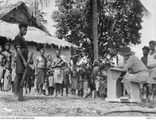 HOPOI, NEW GUINEA, 1943-10-20. NX155085 CAPTAIN R.G. ORMSBY (1) OF THE AUSTRALIAN AND NEW GUINEA ADMINISTRATIVE UNIT, RECRUITING NATIVE LABOURERS. ON THE LEFT IS A NATIVE CONSTABLE OF ROYAL PAPUAN ..