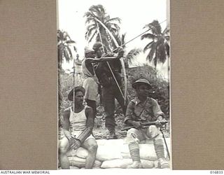1944-04-11. NEW GUINEA. A KAYA-KAYA NATIVE MAN SHOWS AN AUSSIE HOW TO USE A BOW AND ARROW IN DUTCH NEW GUINEA WHILE NEI SOLDIER AND ANOTHER KAYA-KAYA WATCH THE RESULTS