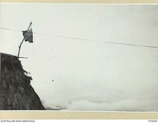 DUMPU, NEW GUINEA. 1944-02-12. THE CONTROL HUT STANDING OUT AGAINST A LEADEN SKY. SLIGHTLY TO THE RIGHT OF AND IN LINE WITH THE ROOFTOP OF THE HUT 12 B25'S (MITCHELL MEDIUM BOMBERS) ARE JUST ..