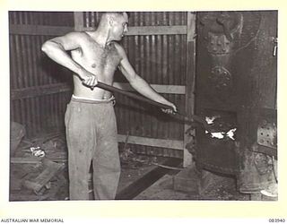 LAE, NEW GUINEA. 1944-12-12. WARRANT OFFICER II W.F. LOY, ARMY CANTEENS SERVICE, SECOND IN CHARGE OF A SOFT DRINK FACTORY IN THE LAE BASE SUB-AREA STOKES THE BOILERS WITH COAL FROM THE WRECKED ..