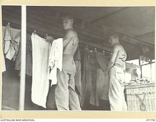 LAE, NEW GUINEA, 1944-03-25. NX177362 PRIVATE J. O. WILSON (LEFT), WITH N206061 PRIVATE V. E. WIGGINS, HANG AND REMOVE CLOTHES IN A CONTINUOUS DRYING ROOM TRAILER AT THE 1ST MOBILE HOSPITAL LAUNDRY ..