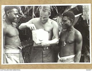 RAMU VALLEY, NEW GUINEA. 1943-12-22. VX23497 SERGEANT A. G. MORTON OF THE 2/31ST AUSTRALIAN INFANTRY BATTALION BEING WATCHED BY ENVIOUS NATIVES AS HE UNPACKS HIS CHRISTMAS PARCEL