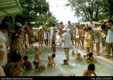 Large group of children swimming in a wading pool, adults supervising