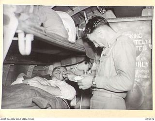 AIRBORNE, LAE, NEW GUINEA TO TOWNSVILLE, 1945-11-26. SERGEANT P.S. WILLIAMS, MEDICAL ORDERLY, TAKING THE TEMPERATURE OF PRIVATE A.R. BYRON, A PATIENT OF 2/7 GENERAL HOSPITAL WHO IS BEING EVACUATED ..