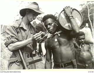 1943-06-28. NEW GUINEA. WAU-MUBO AREA. NATIVE CARRIERS SET OUT ALONG THE TRACK TO FORWARD AREAS. PTE. ALLAN SHORT, OF VICTORIA, SHARES HIS MATCH WITH A NATIVE CARRIER. (NEGATIVE BY G. SHORT)