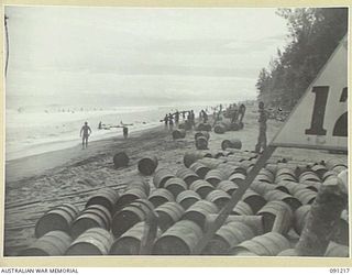 BOUGAINVILLE. 1945-04-25. NATIVES ROLLING 44-GALLON DRUMS OF FUEL ASHORE AFTER THEY HAD BEEN UNLOADED FROM BARGES INTO HEAVY SURF. A 300-TON VESSEL OF 13 SMALL SHIPS COMPANY TRANSPORTED 1200 DRUMS ..